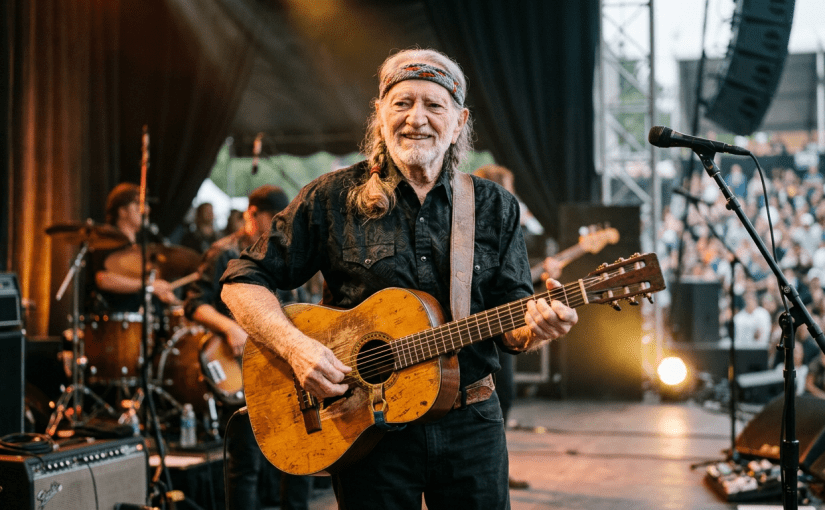 Older man playing an acoustic guitar on stage at a concert